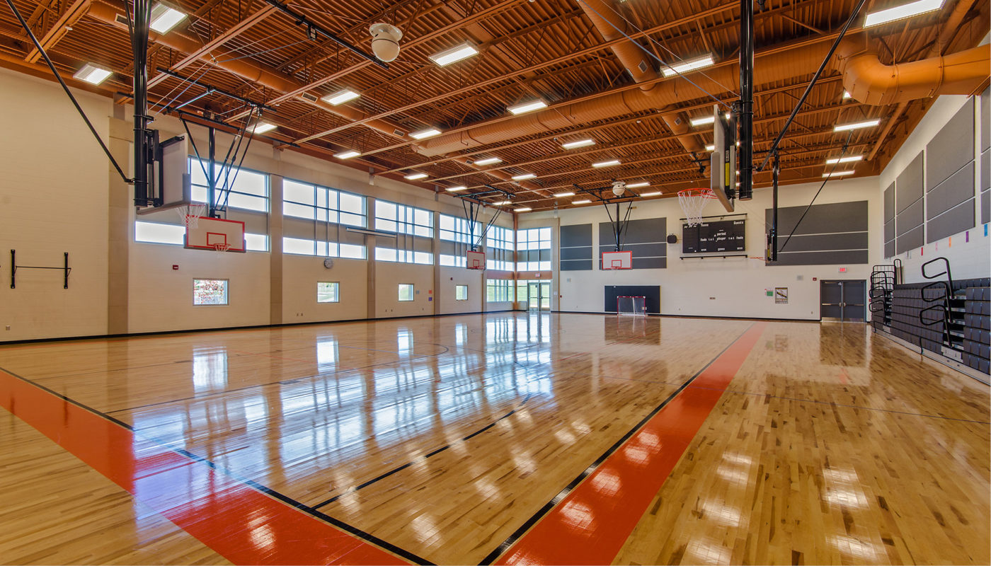 An empty basketball court at Nokesville K-8 School with wooden floors and windows.