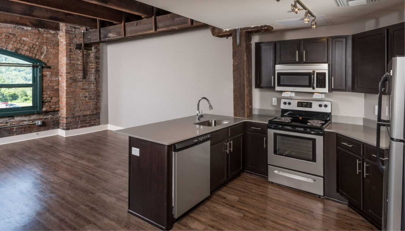 A kitchen with stainless steel appliances and brick walls at Boury Lofts.