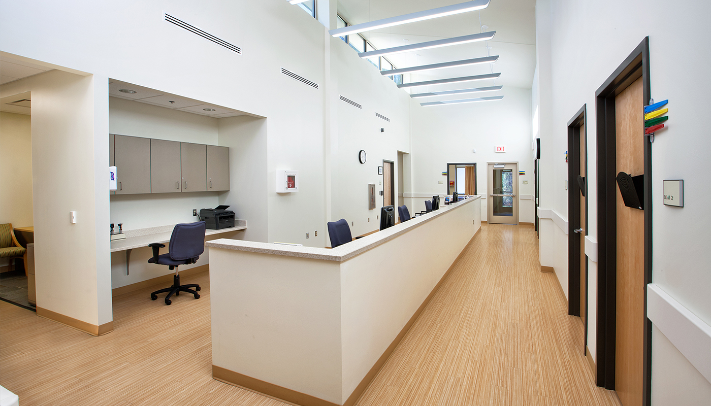 A hallway in a medical office with a desk and chairs.