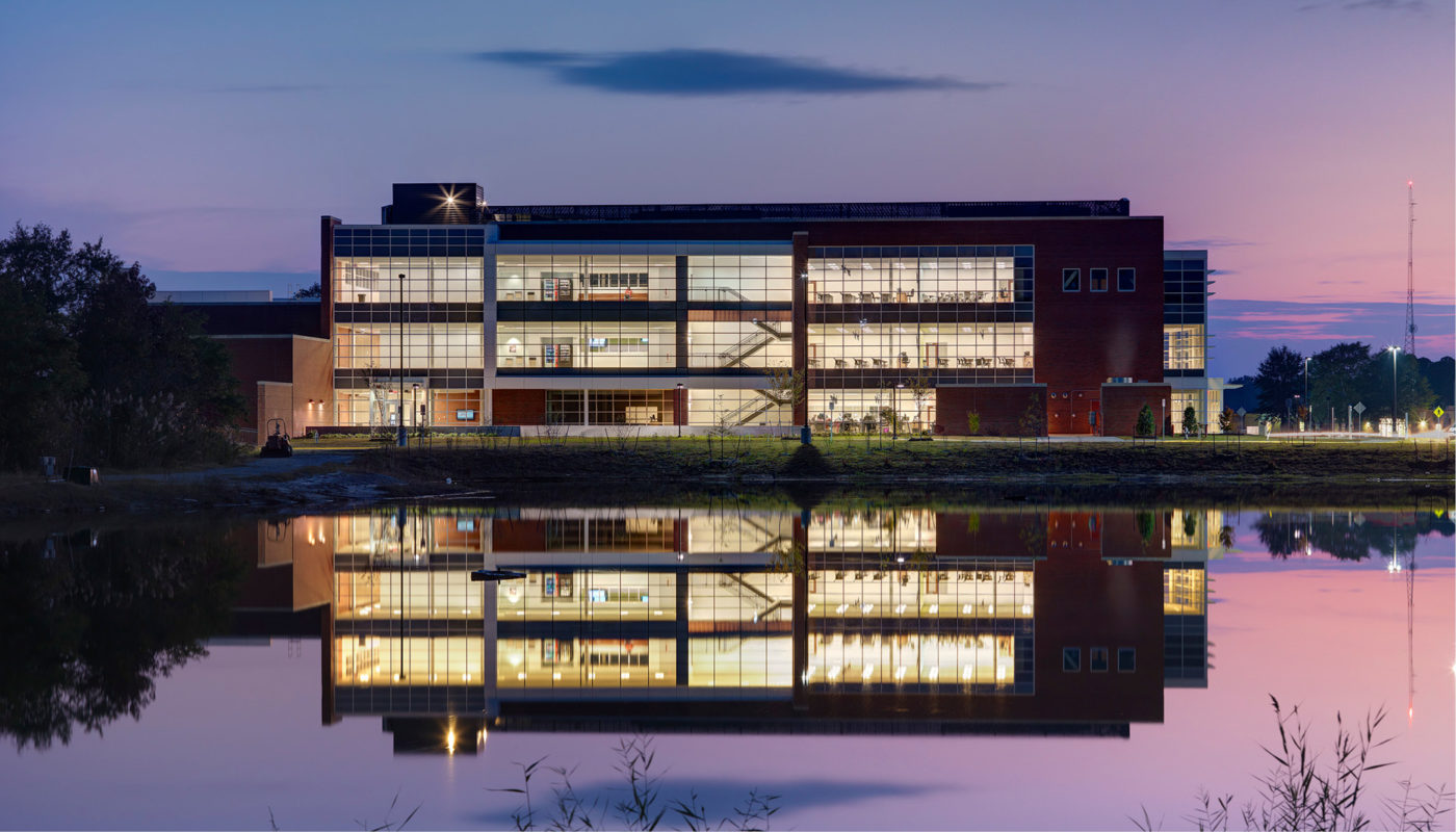 A building is reflected in a body of water at dusk.