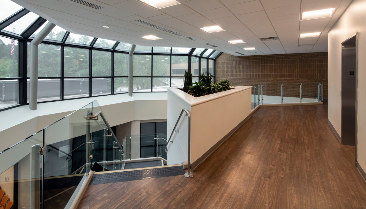 A hallway in an office with glass walls and wood flooring.