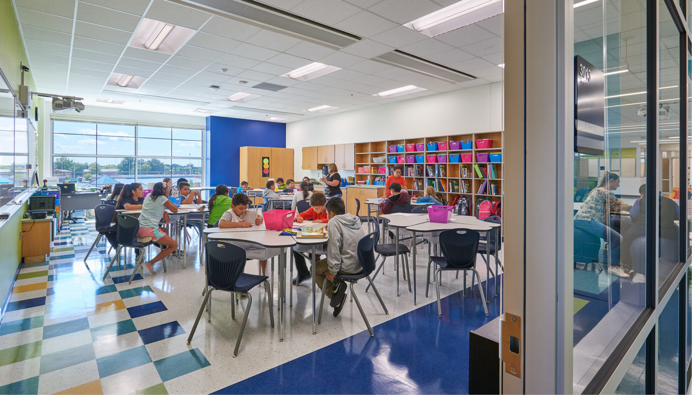 Students at Baldwin Elementary, an intermediate school in Manassas City Public Schools, are sitting at tables in a school library.