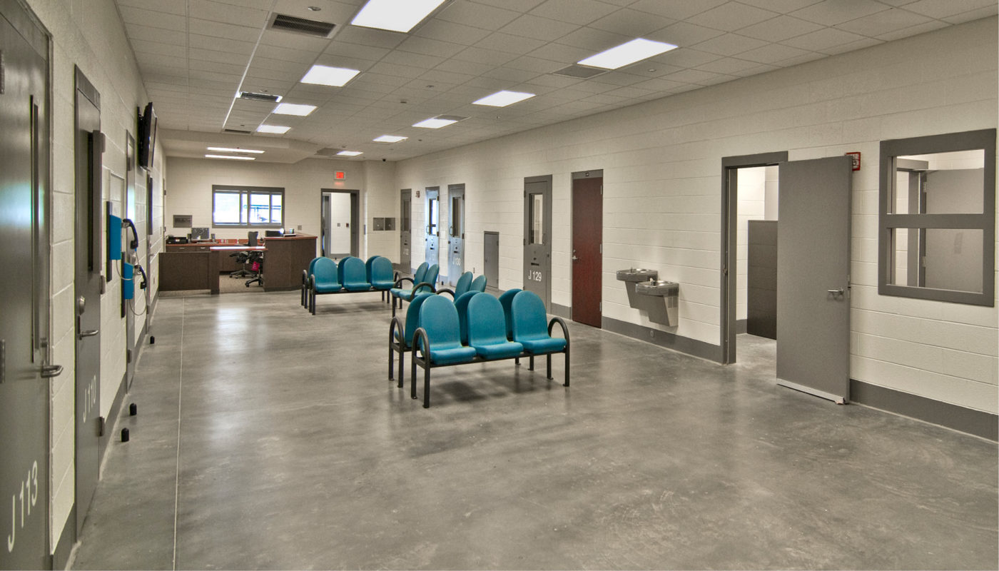 The Rockingham County Detention Center features a hallway with blue chairs and a concrete floor.