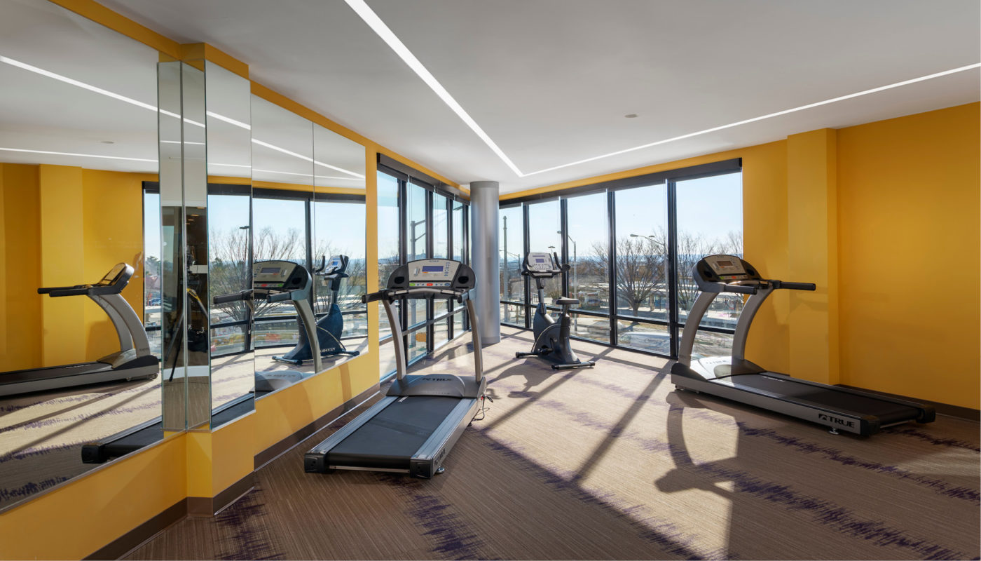 A gym in Metro Heights with yellow walls and tread machines.