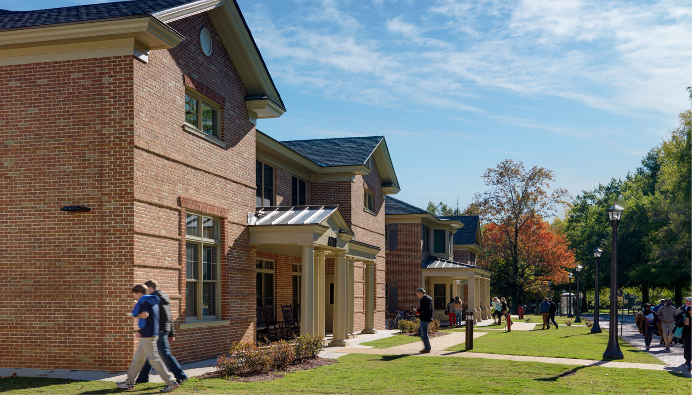 A group of Greek students walking down a sidewalk in front of a brick building at the College of William and Mary's Fraternity Housing Complex.