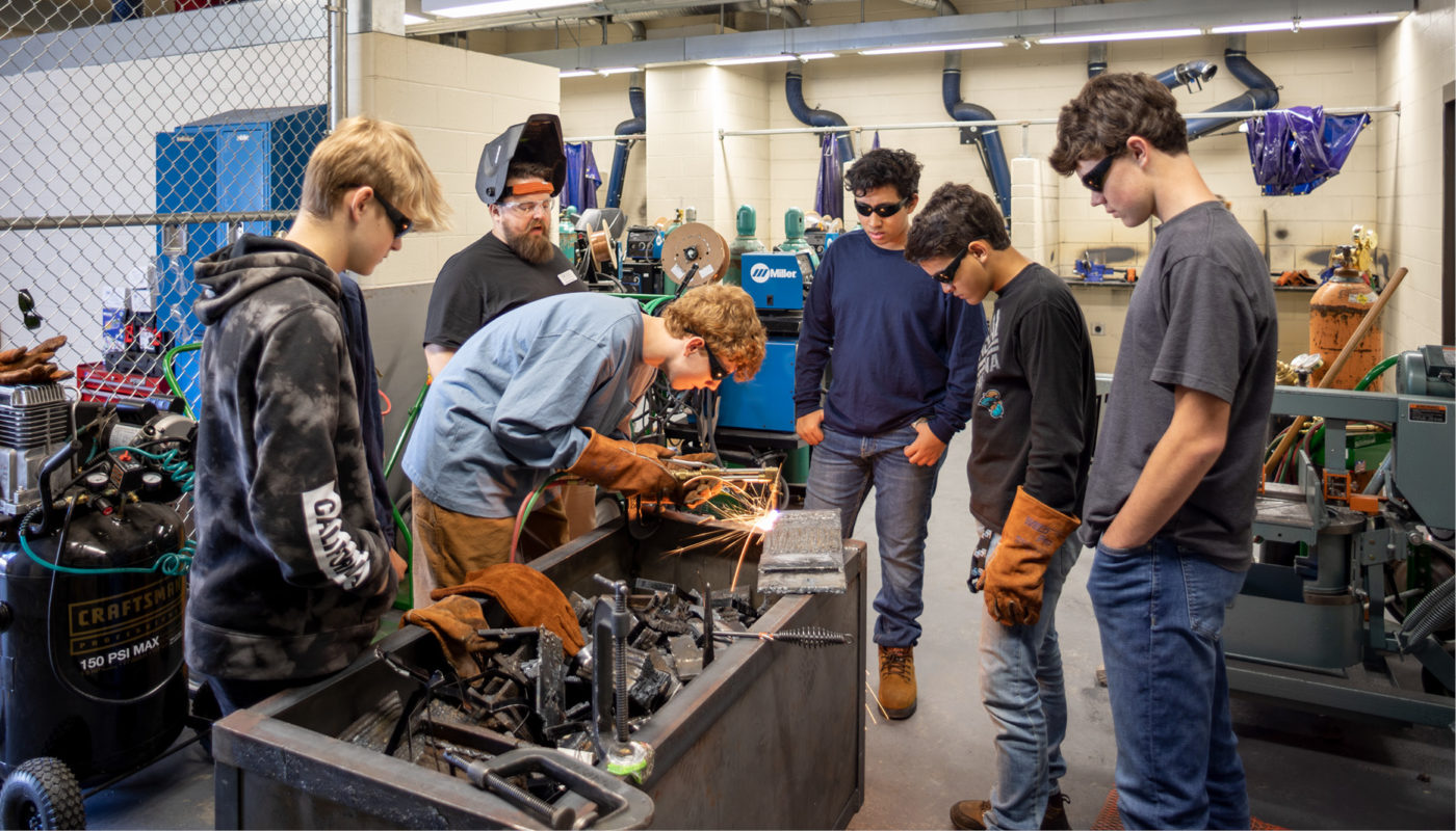 A group of students from Oak Grove High School working on a machine in a workshop.