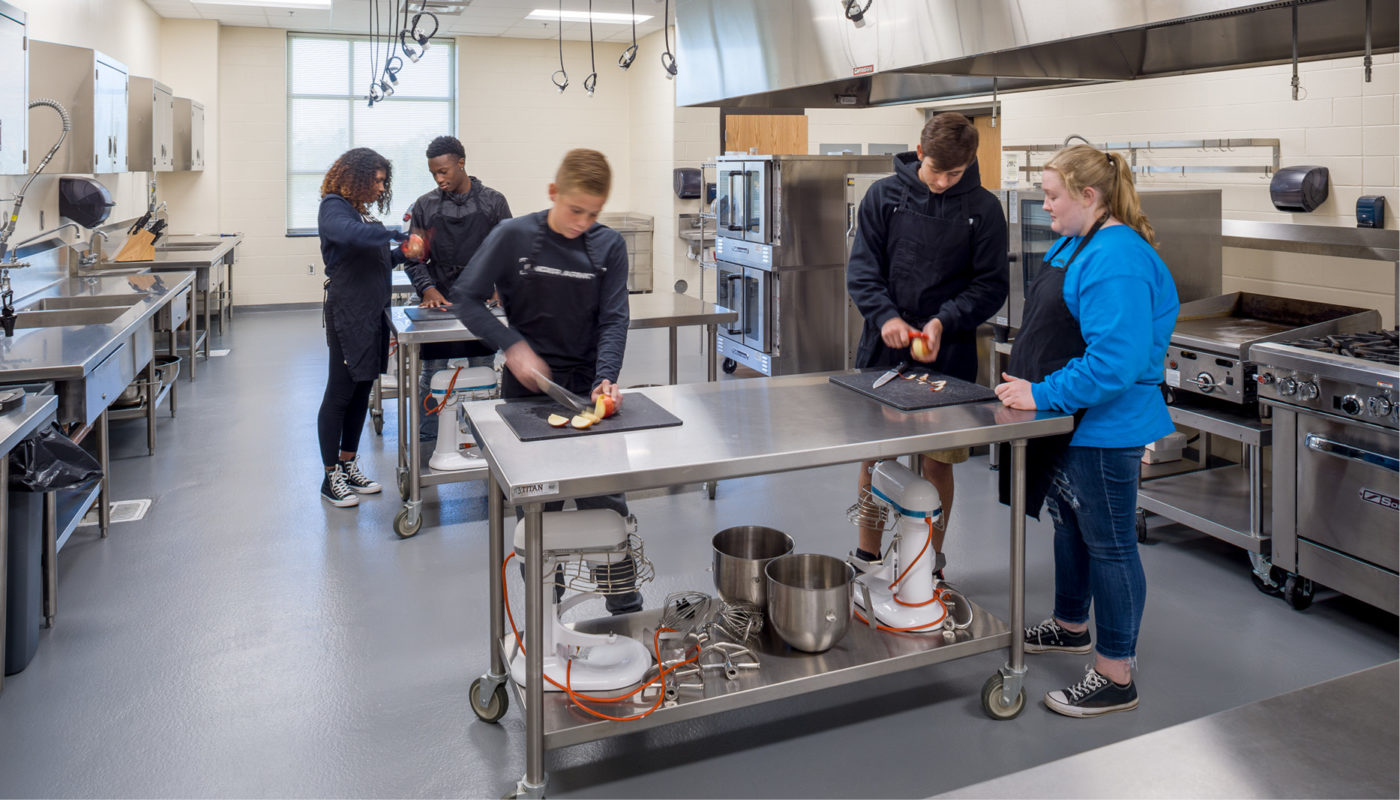 A group of people, including students from Oak Grove High School, in a kitchen preparing food for an event organized by Davidson County Schools.