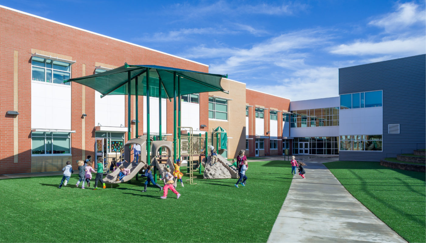 A playground with children from Cherry Park Elementary School playing on the grass in front of a building.