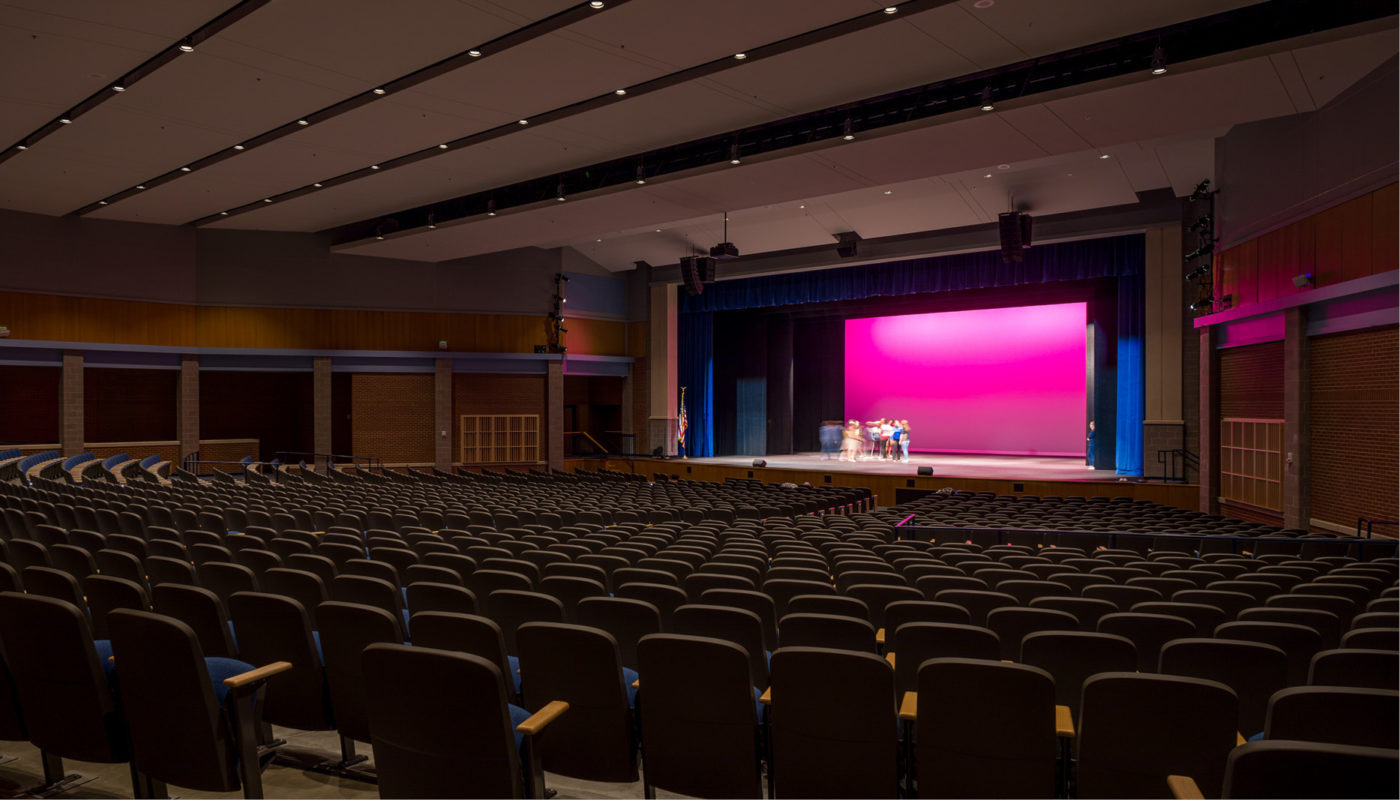 A large auditorium with rows of seats and a stage, located within the Mooresville High School in the Mooresville Graded School District.