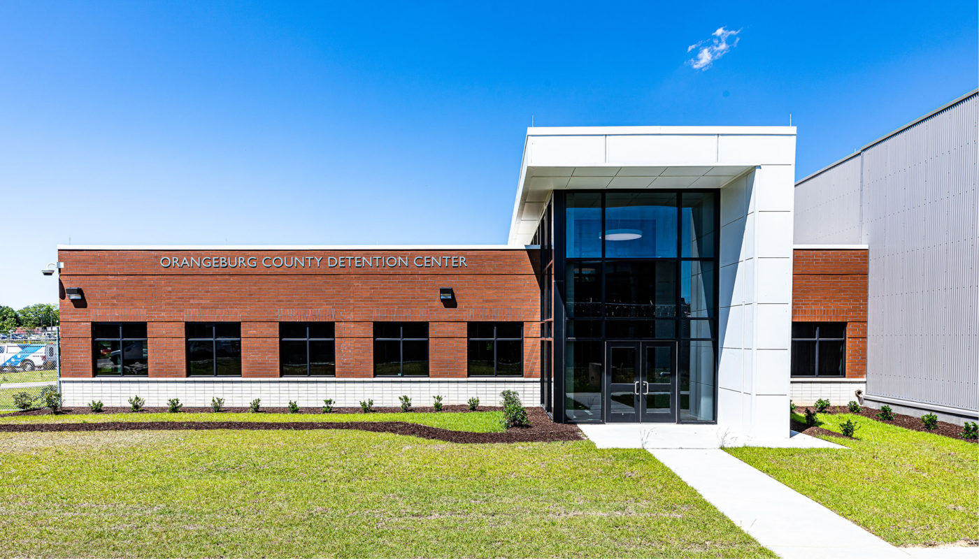 The Orangeburg County Detention Center is a brick building situated in a serene location with a grassy area in front of it.
