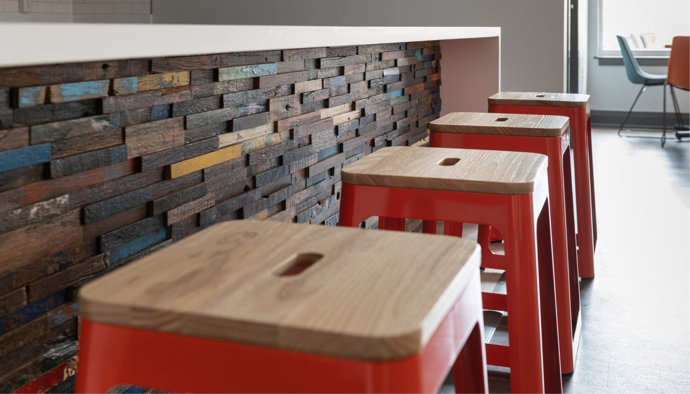 Four red stools in front of a wooden wall.