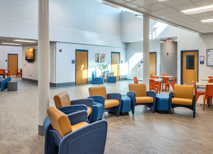 A spacious room with blue chairs and tables, designed with elements of juvenile detention center architecture.