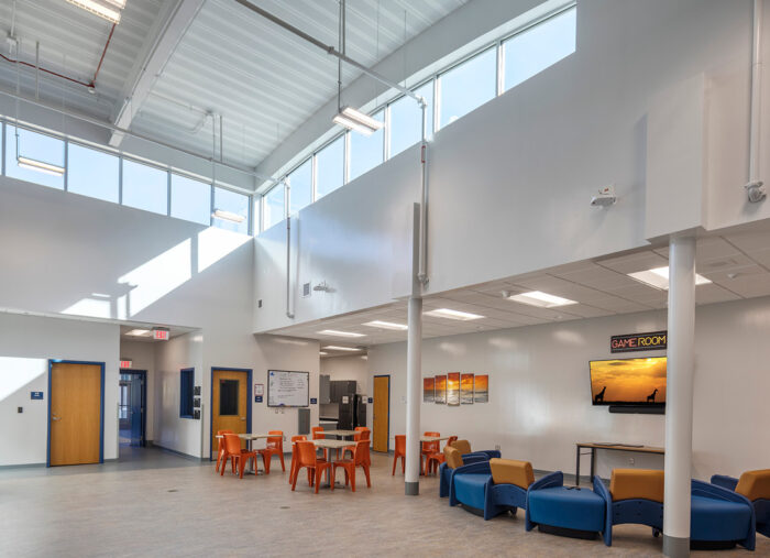 The lobby of a school with blue chairs and a large window designed with juvenile detention architecture principles.