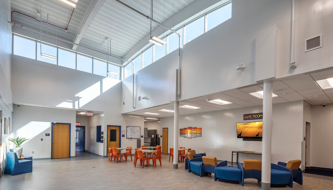 The lobby of a school with blue chairs and a large window designed with juvenile detention architecture principles.