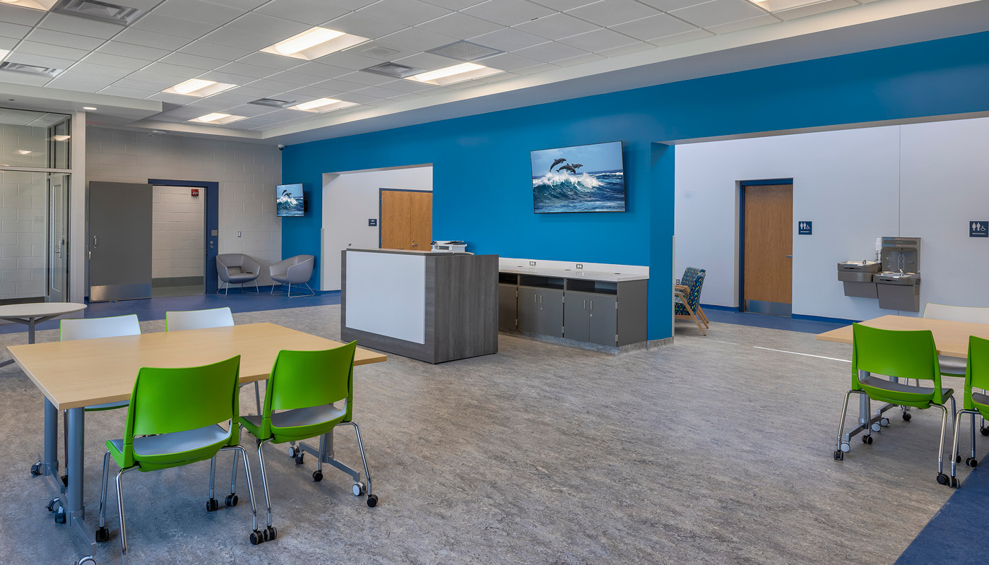 A blue and green room with tables and chairs designed for a juvenile detention center.